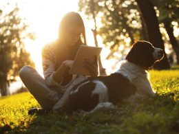 alt="woman enjoying the sun outdoors in sunset with dog using tablet"/>