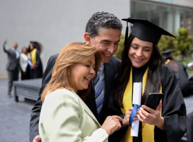 Happy graduating student taking a picture with her parents and looking at the result on her cell phone