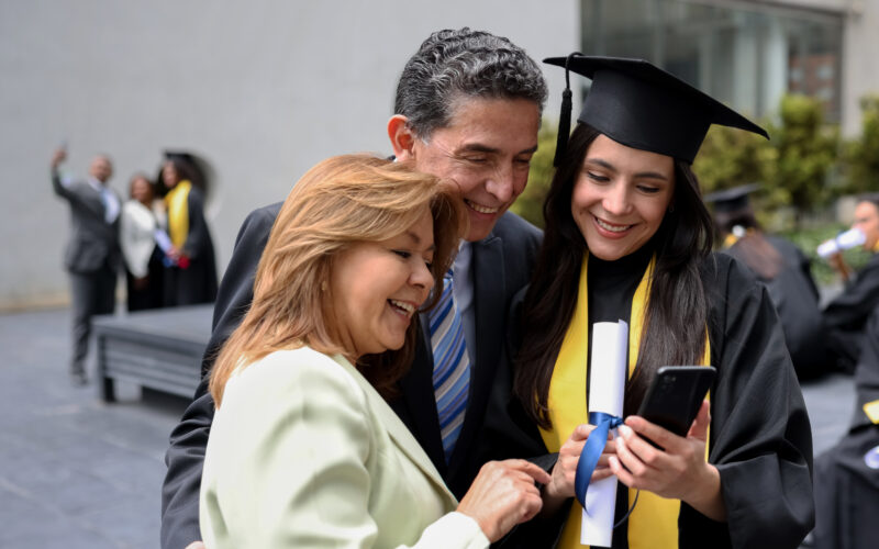 Happy graduating student taking a picture with her parents and looking at the result on her cell phone