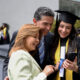 Happy graduating student taking a picture with her parents and looking at the result on her cell phone