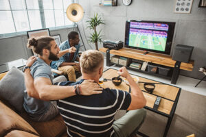 Diverse group of men watching soccer match at home and cheering for favorite team.