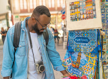 Young african american traveller man with camera choosing the souvenirs at a souvenir shop in Portugal.