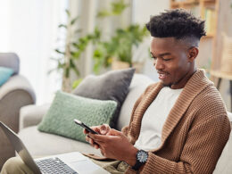Young man typing on smartphone with laptop working from home