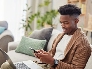 Young man typing on smartphone with laptop working from home