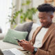 Young man typing on smartphone with laptop working from home