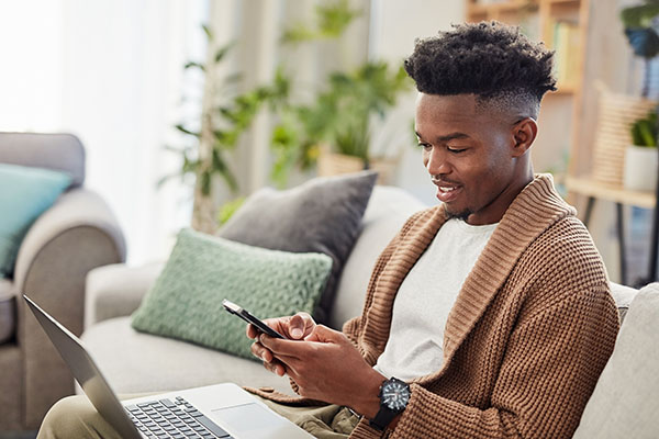 Young man typing on smartphone with laptop working from home