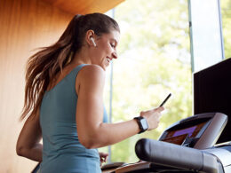 Woman Exercising On Treadmill Wearing Wireless Earphones And Smart Watch Checking Mobile Phone
