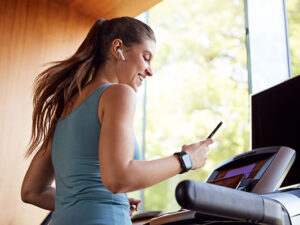 Woman Exercising On Treadmill Wearing Wireless Earphones And Smart Watch Checking Mobile Phone