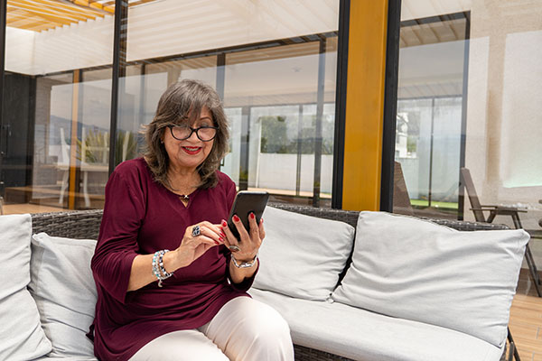 Senior Latin woman looking amused at her cell phone during a relaxing moment on the terrace in the morning