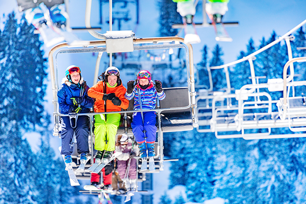Three girls in colorful outfits sit on ski lift talking and smiling together lifting on top of the mountain