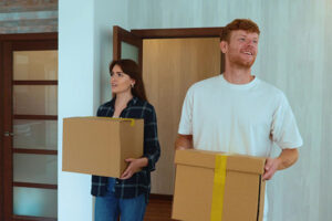 Portrait of Caucasian cheerful young couple in good mood entering their new apartment holding boxes in hands and putting them down on the floor.