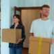 Portrait of Caucasian cheerful young couple in good mood entering their new apartment holding boxes in hands and putting them down on the floor.