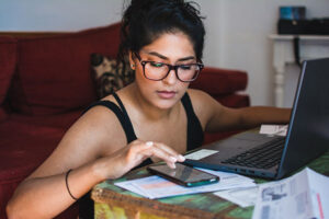 Latina woman working on her personal finances, with her bank statements, bills and computer.