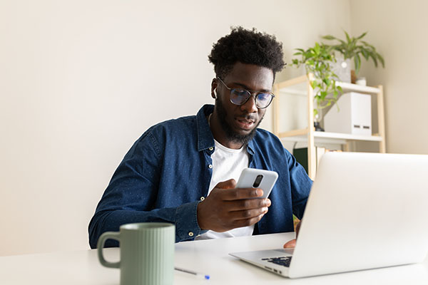 Black man using phone and wireless earphones working at home office.