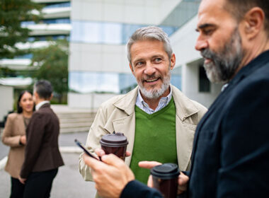 Mature men coworkers smiling and chatting outside office