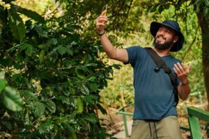 Happy bearded traveler taking a selfie with smartphone on a lush tropical forest trail