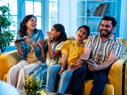 Indian young family playing video game at home on sofa enjoying bonding time