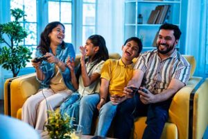 Indian young family playing video game at home on sofa enjoying bonding time