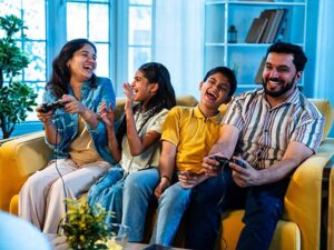 Indian young family playing video game at home on sofa enjoying bonding time