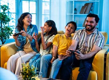 Indian young family playing video game at home on sofa enjoying bonding time