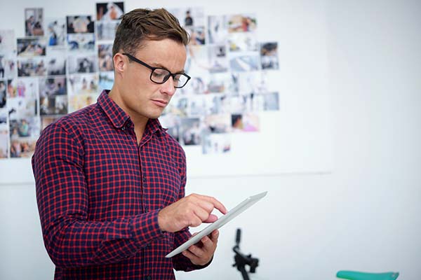 Serious young photographer with tablet computer uploading new photos on social media