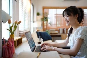 Female specialist working on laptop computer at cozy home living room while sitting at a table.
