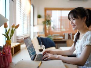 Female specialist working on laptop computer at cozy home living room while sitting at a table.