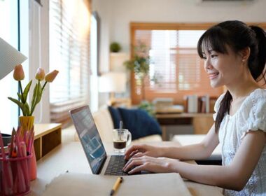 Female specialist working on laptop computer at cozy home living room while sitting at a table.