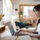 Female specialist working on laptop computer at cozy home living room while sitting at a table.