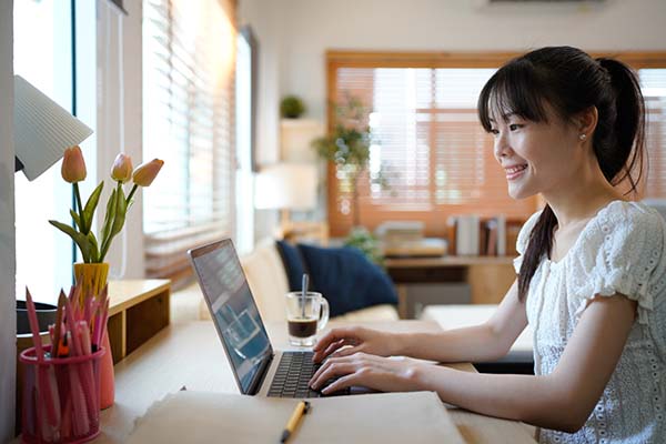 Female specialist working on laptop computer at cozy home living room while sitting at a table.