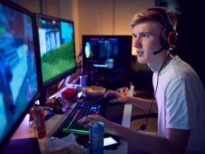 Teenage boy wearing headset gaming at home using dual computer screens