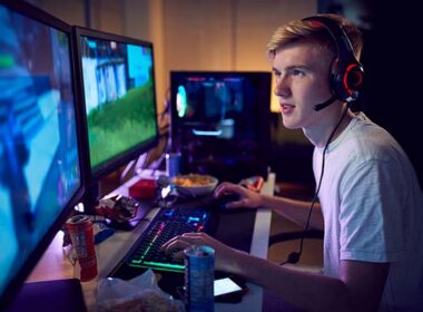 Teenage boy wearing headset gaming at home using dual computer screens