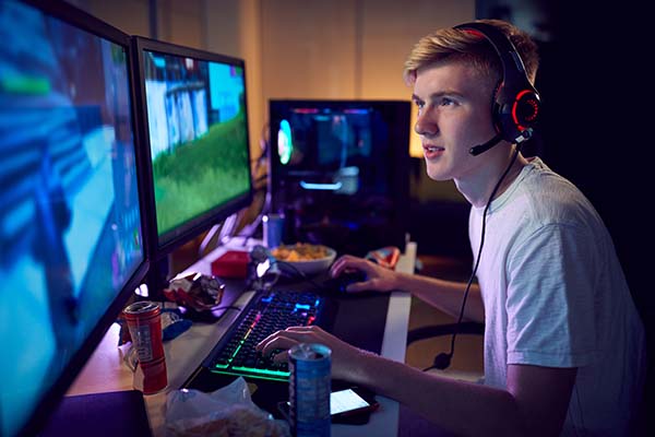 Teenage boy wearing headset gaming at home using dual computer screens